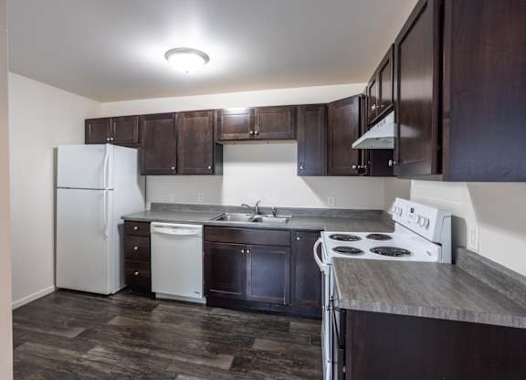 an empty kitchen with dark wood cabinets and white appliances