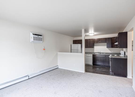 an empty living room with a kitchen in the background