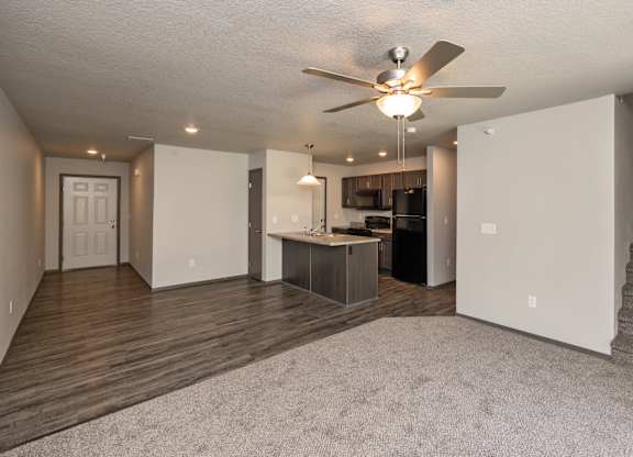 A spacious living room with a ceiling fan and a staircase.