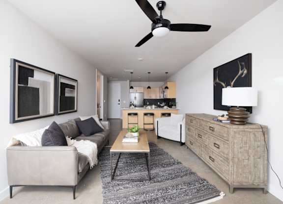 A living room with a grey couch and a black ceiling fan.