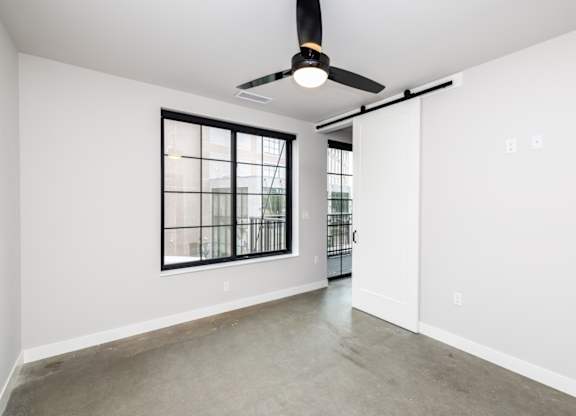 A room with a ceiling fan and a window with bars.