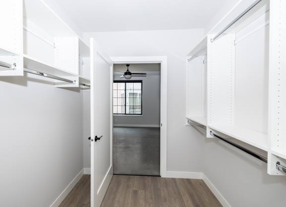a walk in closet with white cabinets and a window