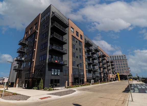 A large, modern apartment building with balconies and a parking lot in front.