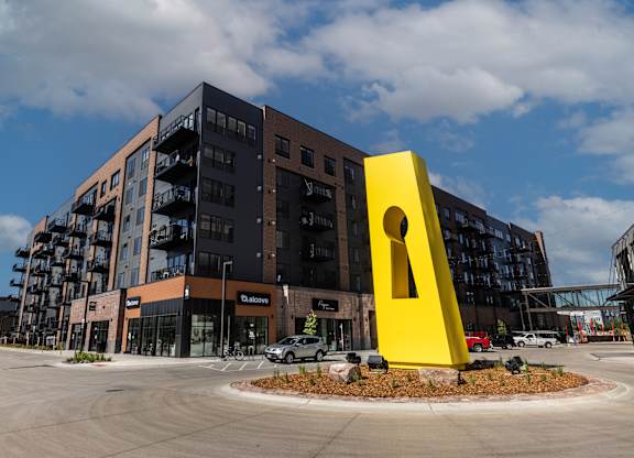 A large yellow keyhole sculpture is in front of a multi-story building.