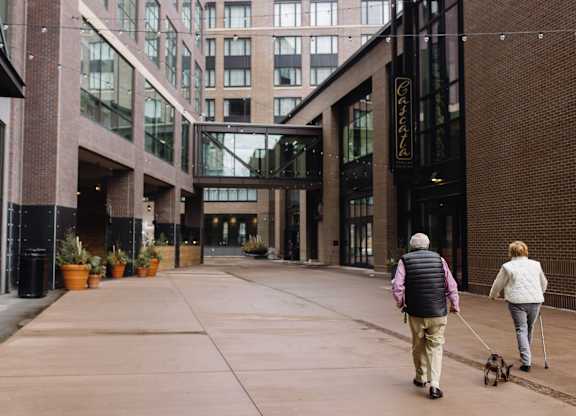 Two people walking a dog in a courtyard.