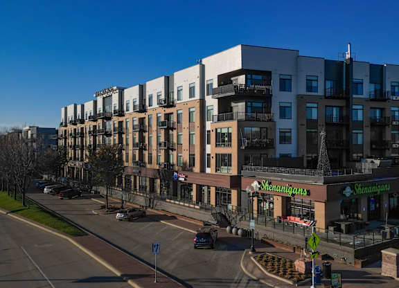 A street view of a residential area with a row of apartment buildings and a green lawn.