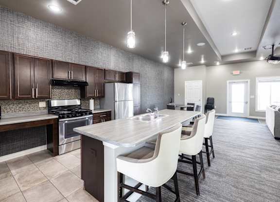 A modern kitchen with a large island and white chairs.