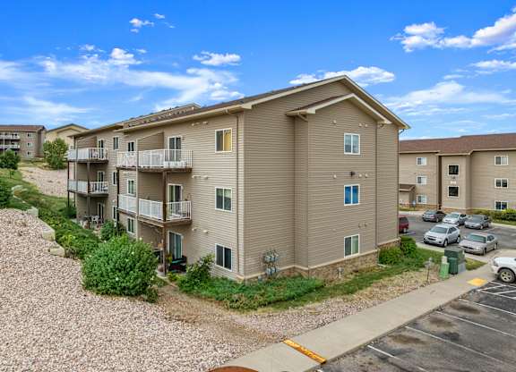 A sunny day at the apartment complex with cars parked in the parking lot.