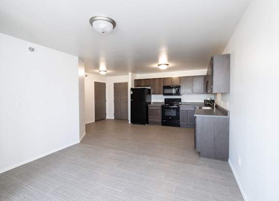 an empty living room and kitchen with black appliances and white walls