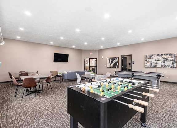 A foosball table is in the middle of a room with chairs and a TV.