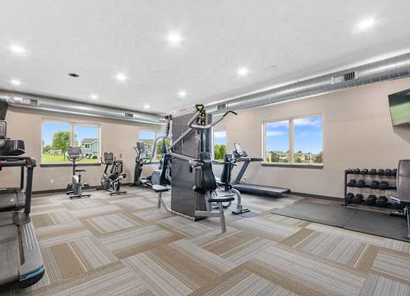 A spacious gym with a variety of equipment and a view of the outdoors through the windows.