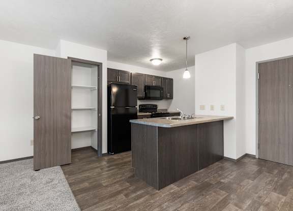 A kitchen with a black fridge and microwave, brown cabinets, and a grey rug.