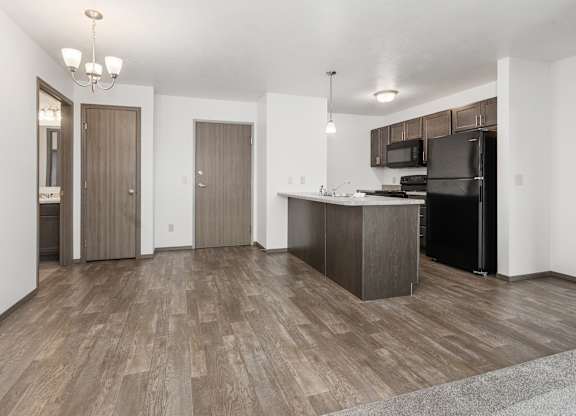 A kitchen with a black refrigerator and wooden floors.