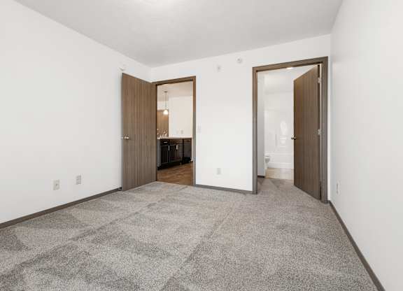 A carpeted room with a white wall and a brown door.