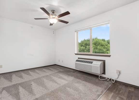 A room with a ceiling fan and a window with an air conditioner unit under it.