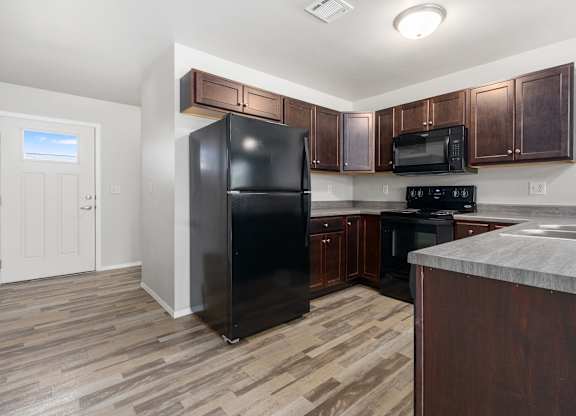 A black refrigerator stands in a kitchen with wooden cabinets and a marble countertop.