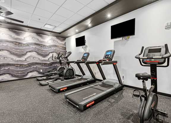 A gym with treadmills, exercise bikes, and a television.