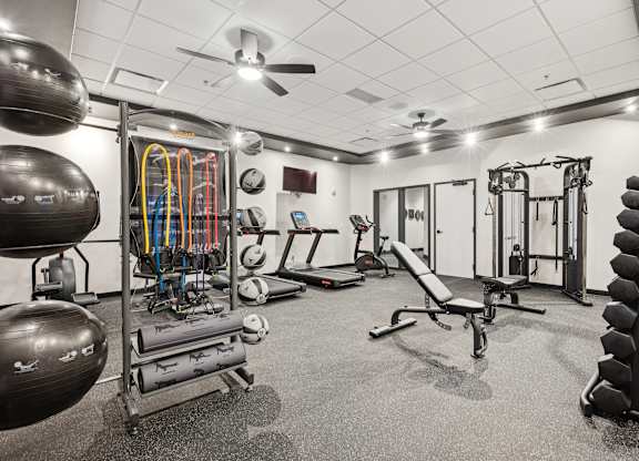 A gym with a variety of equipment including a weight bench, a squat rack, and a rowing machine.