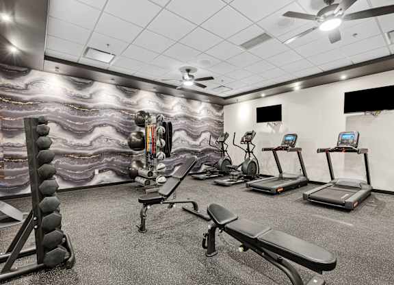 A gym with a variety of equipment including treadmills, a bench, and a weight rack.