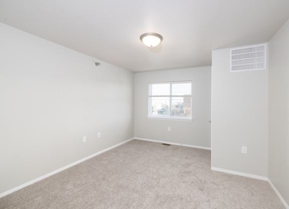 A spacious, empty room with a window and carpeted floor.