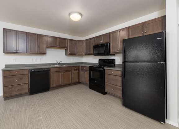 A black refrigerator is in a kitchen with brown cabinets.