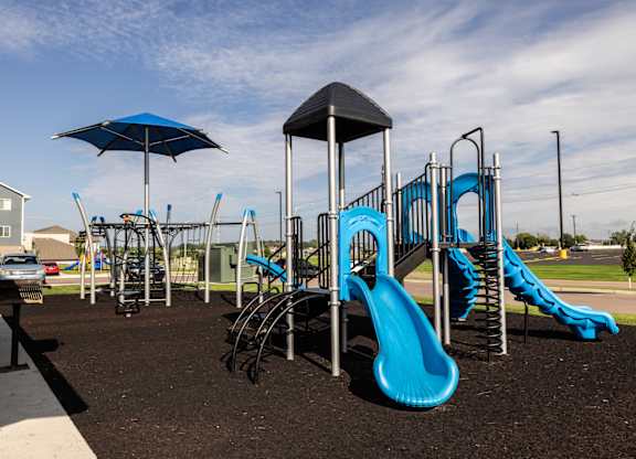 A playground with a blue slide and a black umbrella.