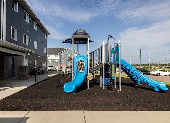 A playground with a blue slide and a black and white building in the background.