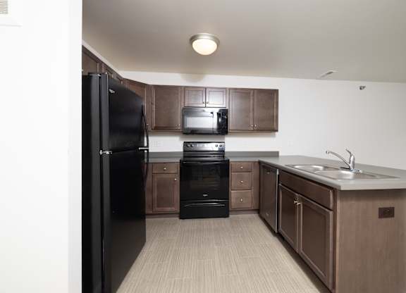 A black refrigerator is in a kitchen with brown cabinets.