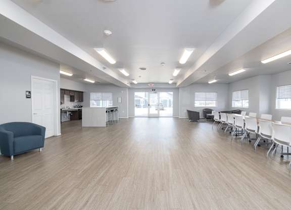 A room with white walls and wooden flooring has a long table with chairs and a speaker.
