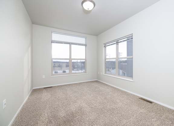 A room with a carpeted floor and two windows.