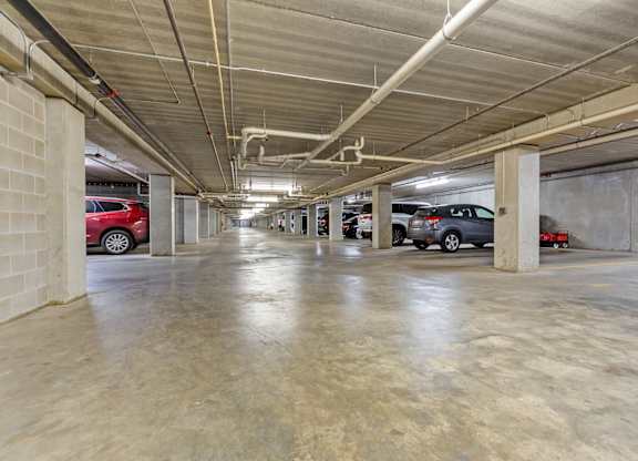 A parking garage with concrete floors and walls, and cars parked in the background.