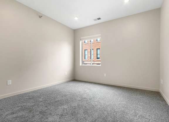 A room with a window and a grey carpet.