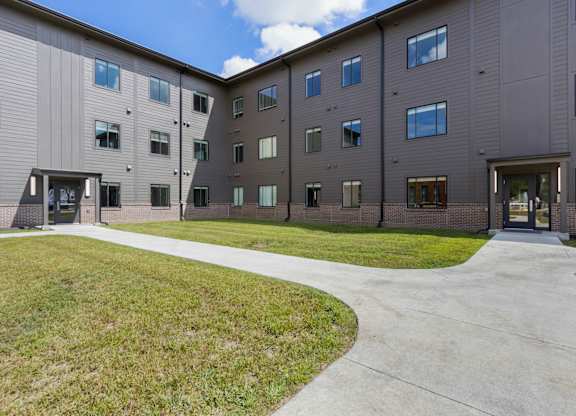 A large building with a grey exterior and a walkway in front.