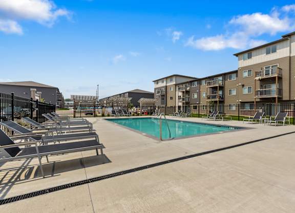 A swimming pool surrounded by sun loungers and apartment buildings.
