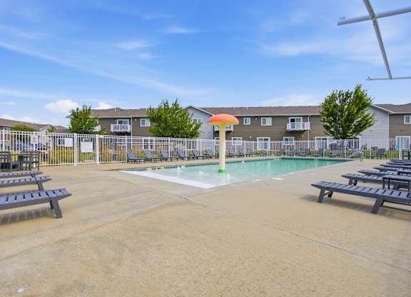 A pool with a slide in the middle of a sandy area with benches.
