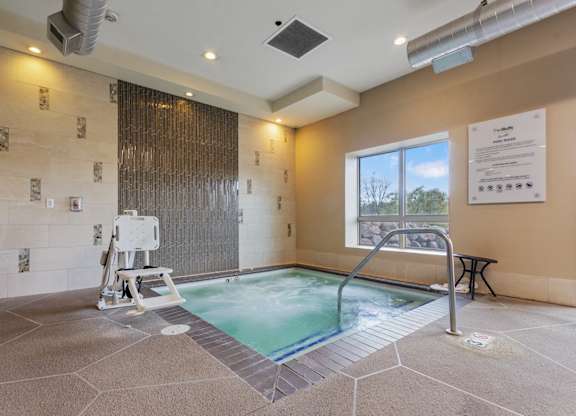 A hot tub in a room with a window and a wall of tiles.