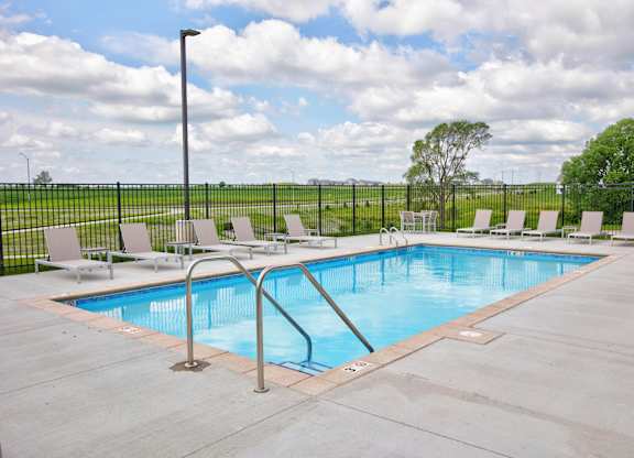 A large outdoor swimming pool surrounded by a metal fence and lounge chairs.