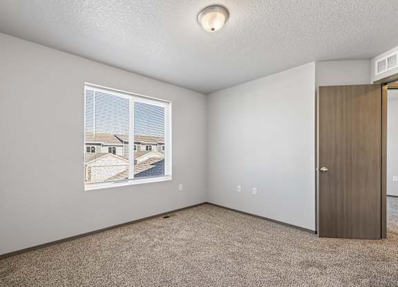 A room with a carpeted floor, a window with blinds, a picture on the wall, and a door.