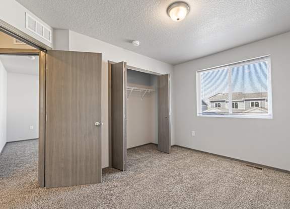 A room with a carpeted floor, a window, and a picture of a house on the wall.
