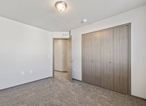 A room with a carpeted floor and a white wall with a door and a wardrobe.