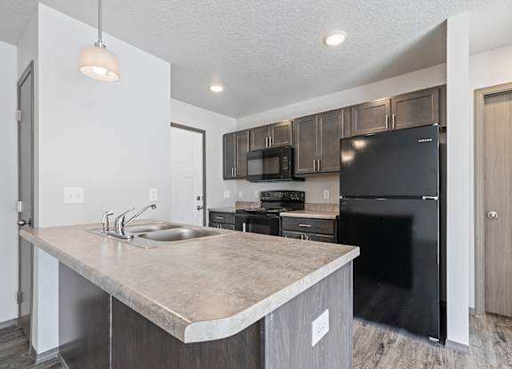 A kitchen with a black refrigerator and a sink with a faucet.