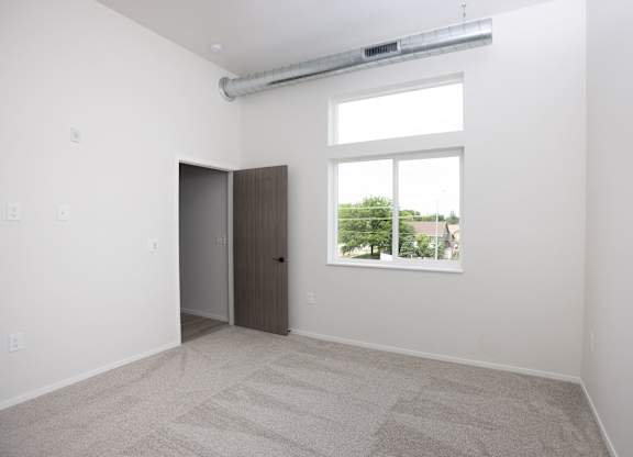 A room with a carpeted floor, a door, and a window.