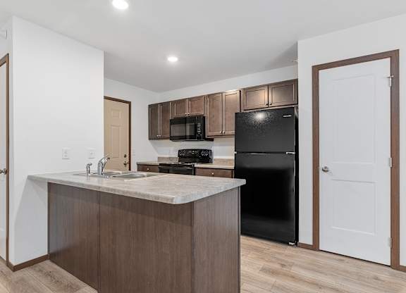 A kitchen with a black refrigerator and brown cabinets.
