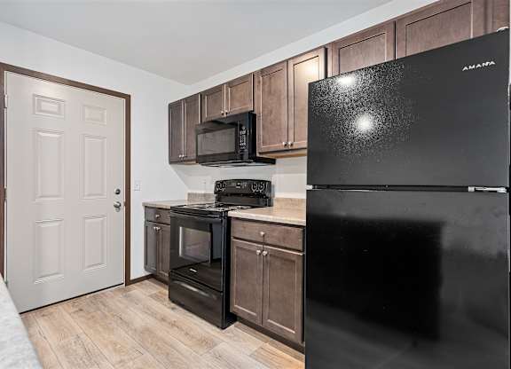 A black fridge in a kitchen with wooden cabinets and a microwave.