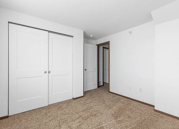 A room with carpeted floor and white walls with a white closet and a door.