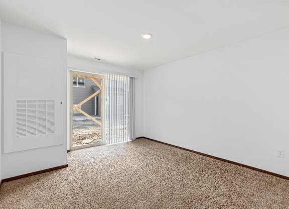 A room with a carpeted floor and a window with blinds.