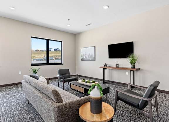 A living room with a grey couch, a black chair, a wooden coffee table, and a flat screen TV mounted on the wall.