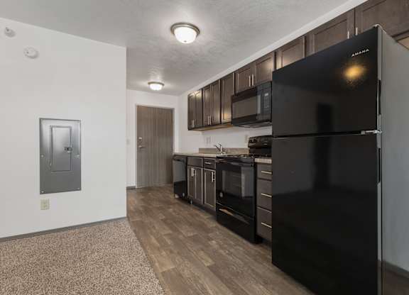 A black refrigerator in a kitchen with wooden floors and cabinets.