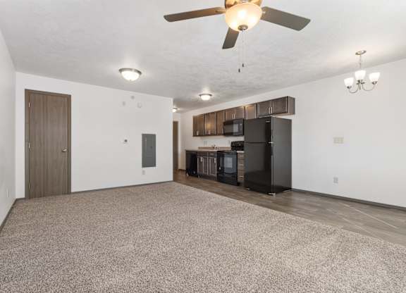 A spacious living room with a ceiling fan and a kitchen area in the background.