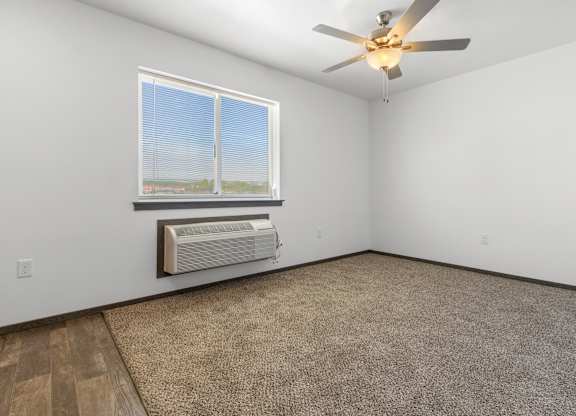 A room with a ceiling fan, carpeted floor, and a window with blinds.